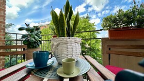 Un balcón con una mesa, una planta en maceta y una taza azul.