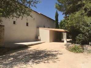 A building with a covered entrance, a gravel driveway, and surrounding greenery. - Gîte “L’Oustalet” with Private Terrace, Wi-Fi, and Air Conditioning (Le Garn)