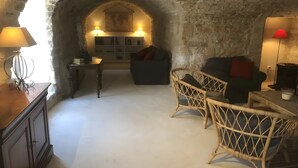A cozy room with a stone archway, a sofa, wicker chairs, and a small table with a lamp. - Gîte "Le Jorance" with Private Terrace, Wi-Fi, and Air Conditioning (Le Garn)