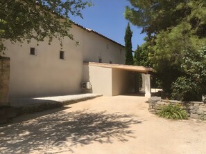 A building with a covered entrance, a gravel driveway, and surrounding greenery. - Gîte "Le Jorance" with Private Terrace, Wi-Fi, and Air Conditioning (Le Garn)
