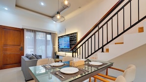 A modern dining area with a glass table, wooden chairs, and a staircase with a black railing. - Villa Sandalwood - Seminyak (Seminyak)