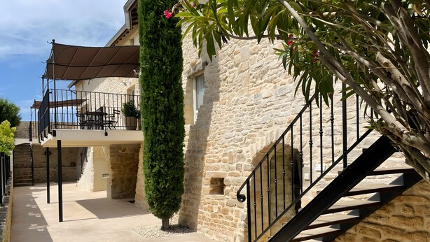 A stone building with a staircase, a balcony, and a covered outdoor seating area.
