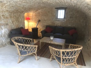 Une pièce chaleureuse aux murs de pierre, avec une cheminée, un canapé, deux fauteuils en osier et une petite table sur laquelle se trouve un verre de lait.