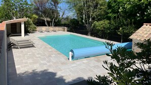 A swimming pool with a tiled deck, lounge chairs, and a stone wall.