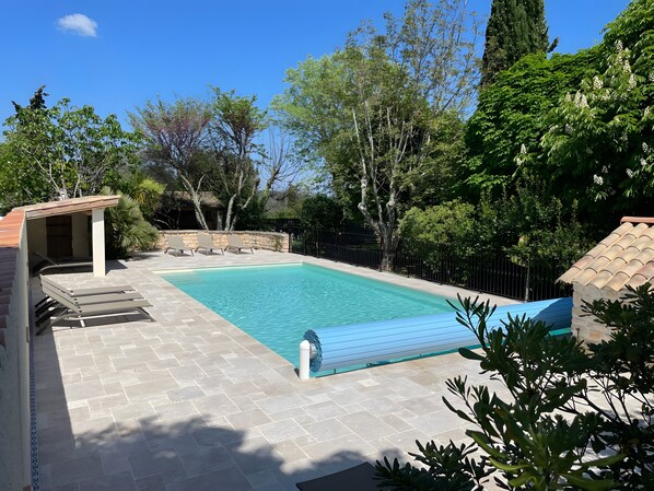 A swimming pool with a tiled deck, lounge chairs, and a stone wall.