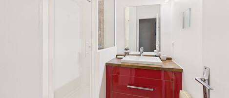 Une salle de bain moderne avec une douche à parois de verre, un meuble-lavabo rouge et un grand miroir.