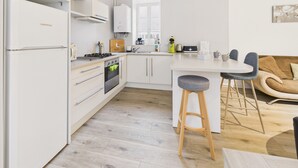 Eine moderne Küche mit weißen Schränken, einem eingebauten Ofen und einem Herd. Es gibt eine Bar mit Hockern und ein braunes Sofa im Essbereich.