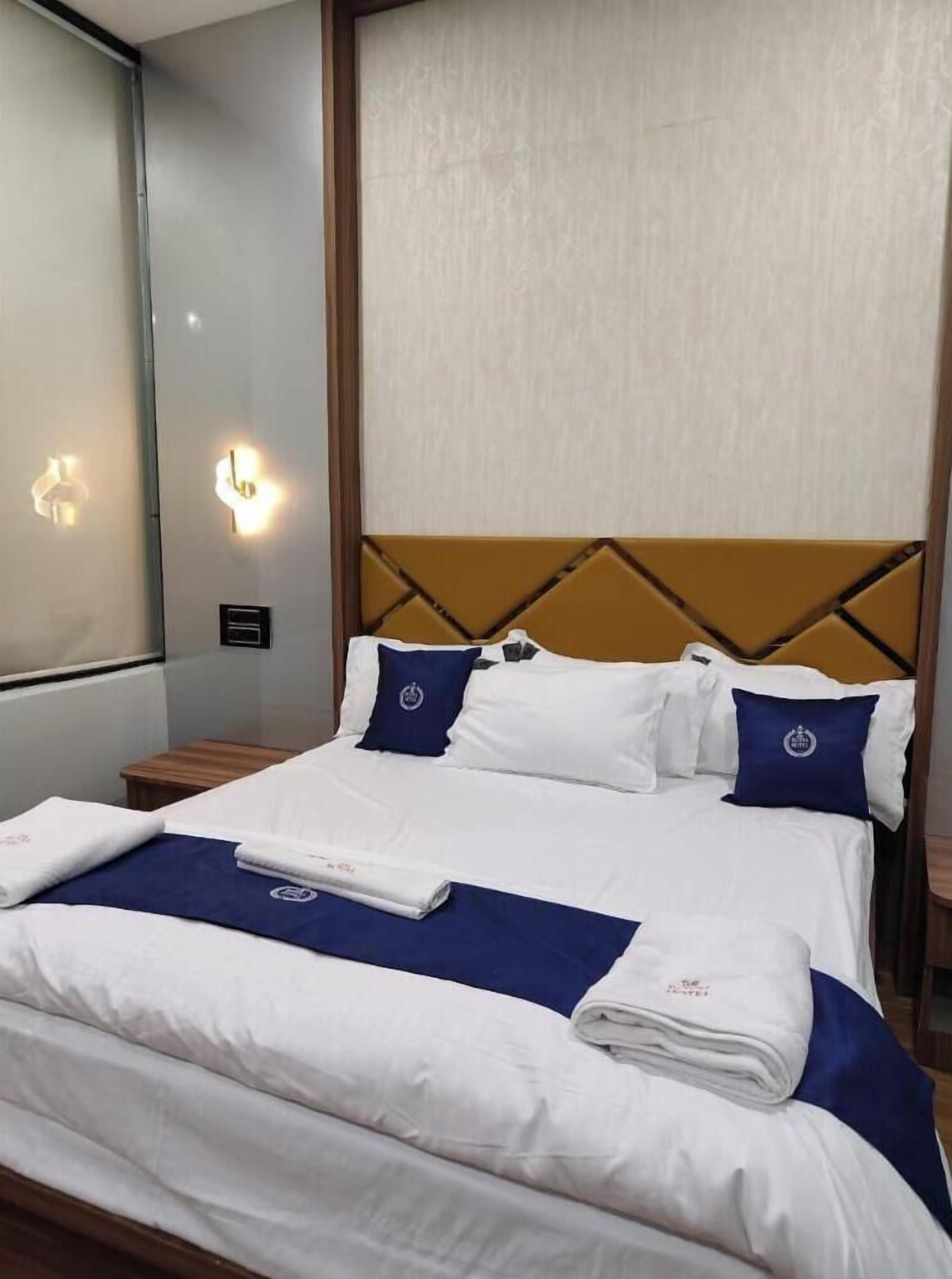 A neatly made bed with white and blue bedding, a headboard with a geometric pattern, and a wall-mounted light fixture.