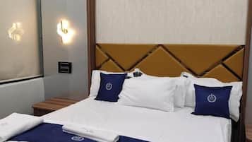 A neatly made bed with white and blue bedding, a headboard with a geometric pattern, and a wall-mounted light fixture.
