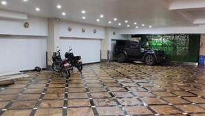 Un amplio estacionamiento interior con piso a cuadros, múltiples luces en el techo y un vehículo grande estacionado al fondo.