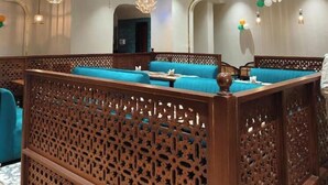 Una habitación de hotel moderna con zona de estar que incluye sofás acolchados azules, paneles decorativos de madera y múltiples lámparas colgantes.