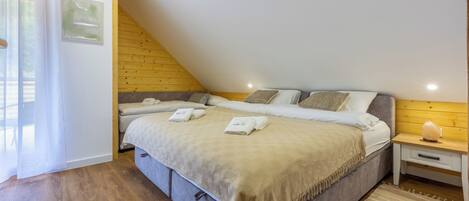A bedroom with a sloped ceiling, a bed with a beige blanket, two bedside tables, and a window with curtains.