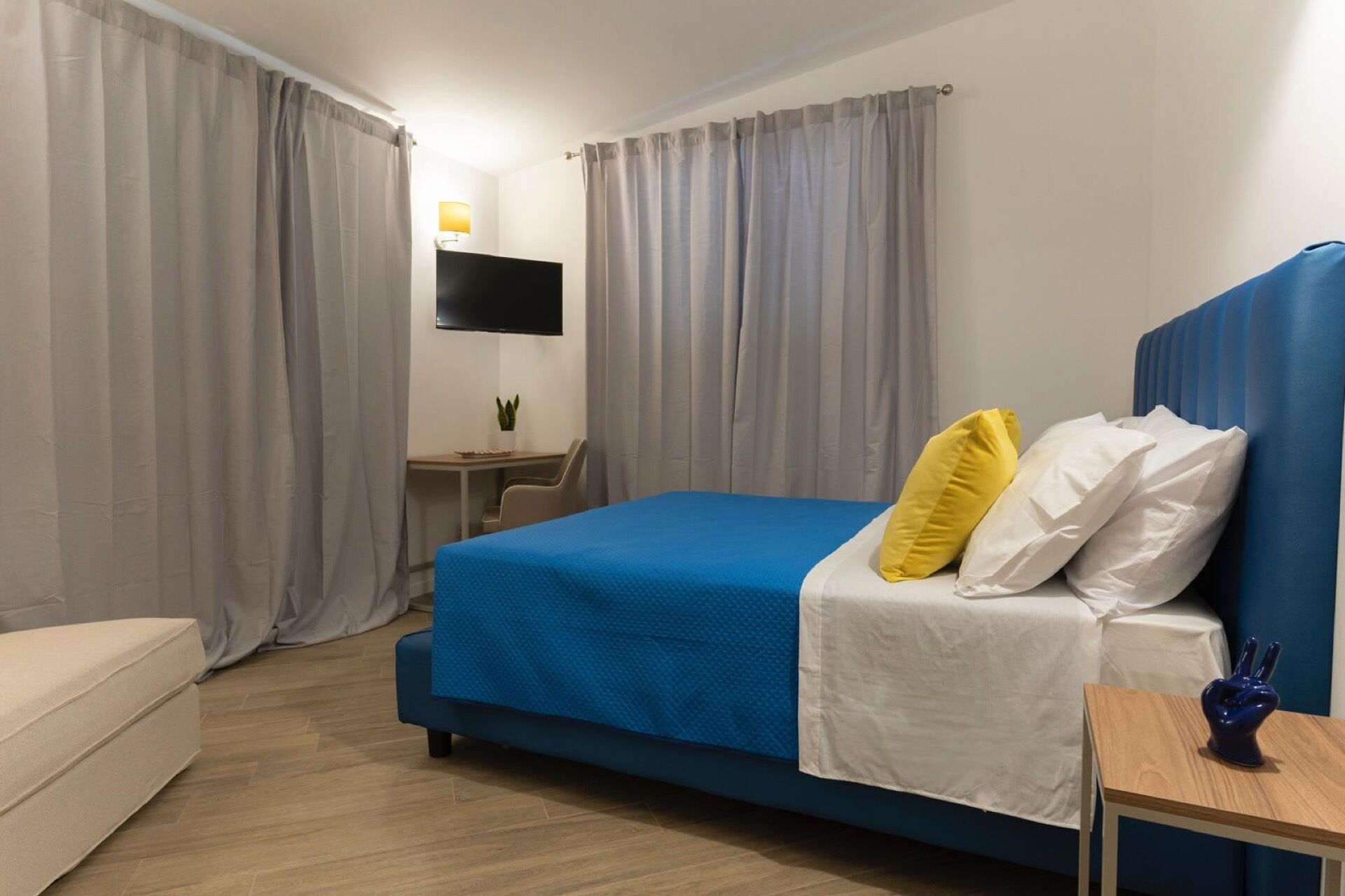 Ein Hotelzimmer mit einem Bett, einem Schreibtisch, einem Stuhl, einem Fernseher und Vorhängen.