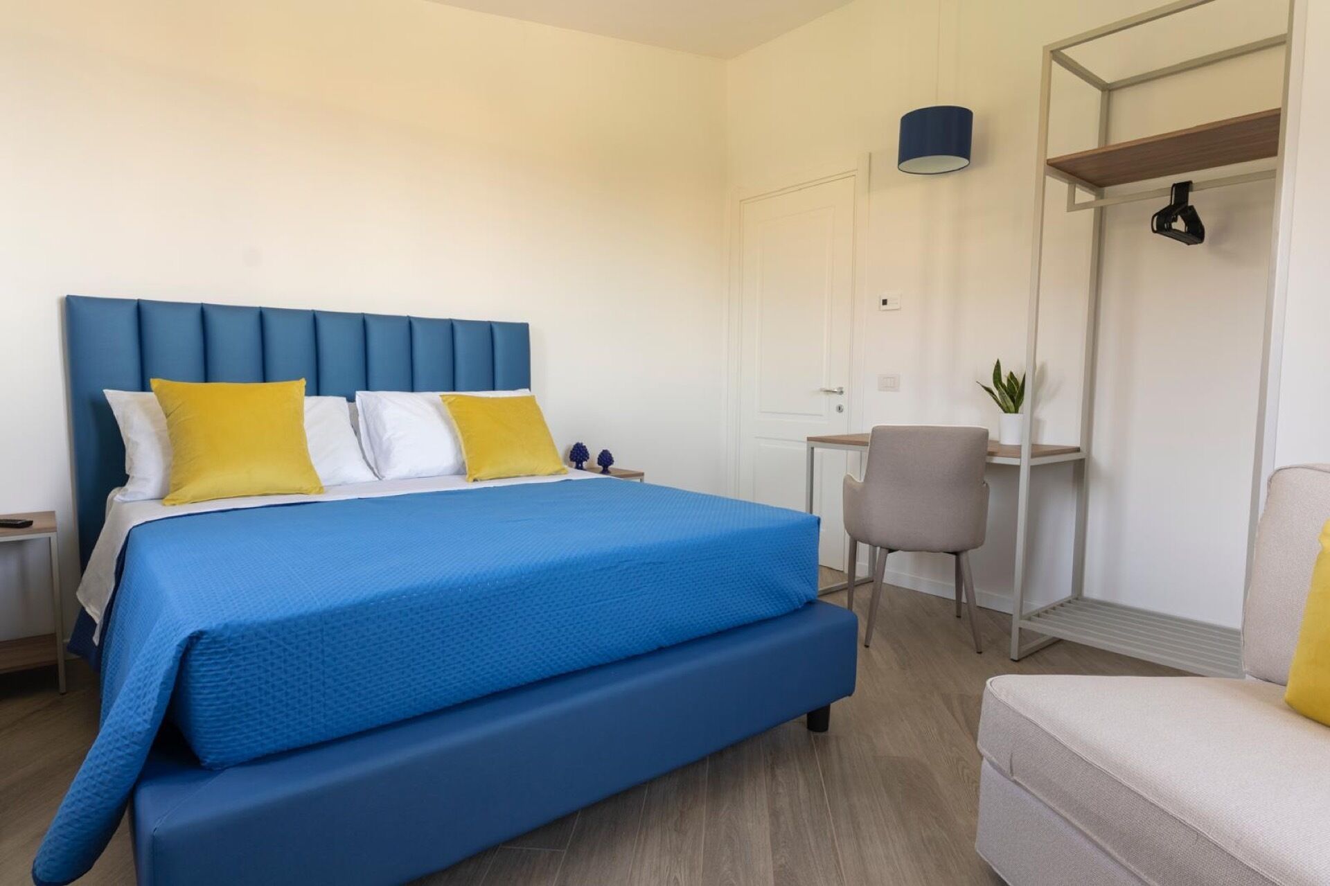A hotel room with a large bed, a desk, a chair, and a wardrobe.