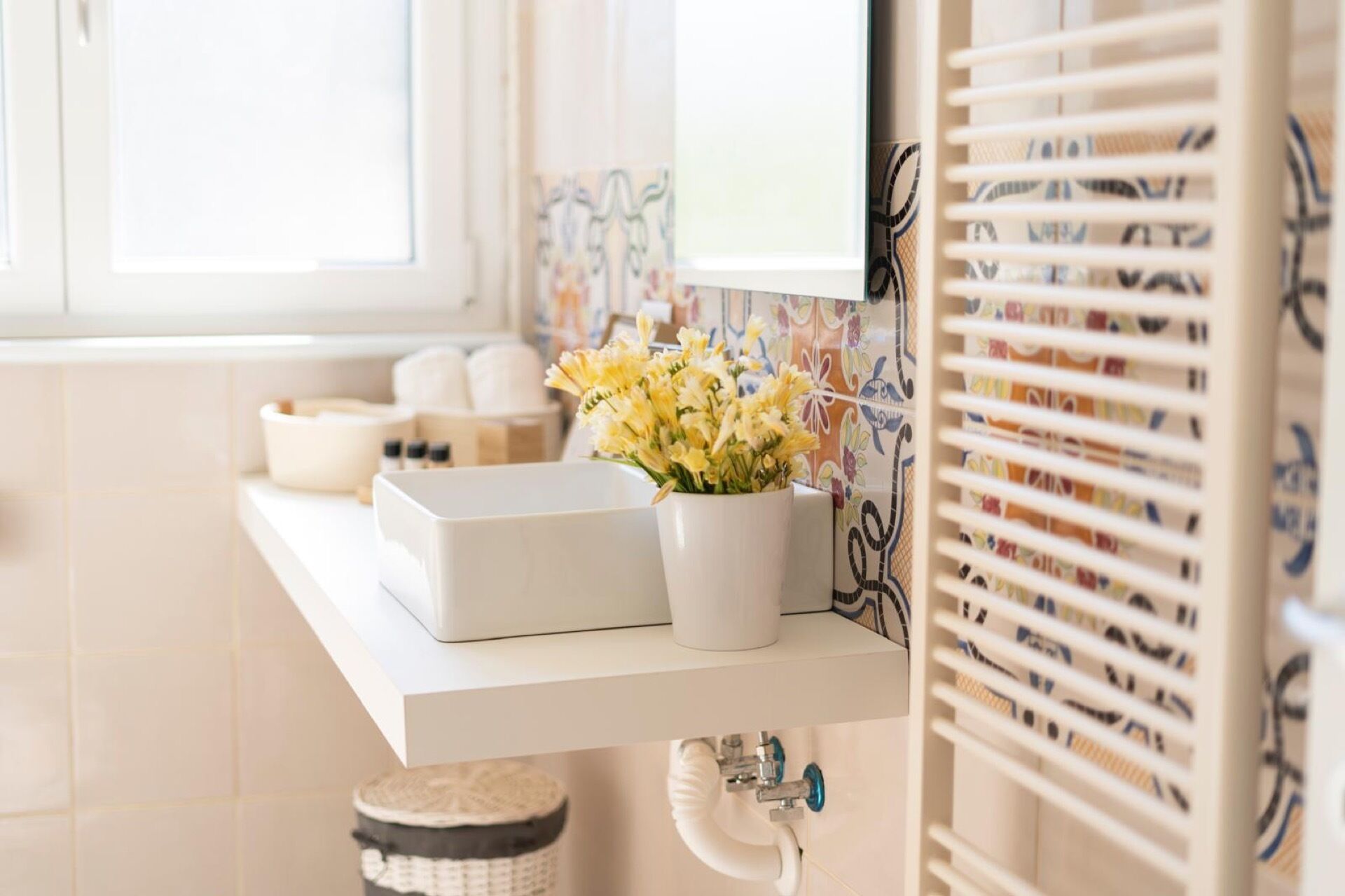 Un bagno con un lavandino bianco, un vaso con fiori gialli e un portascopevoli con asciugamani fantasia.