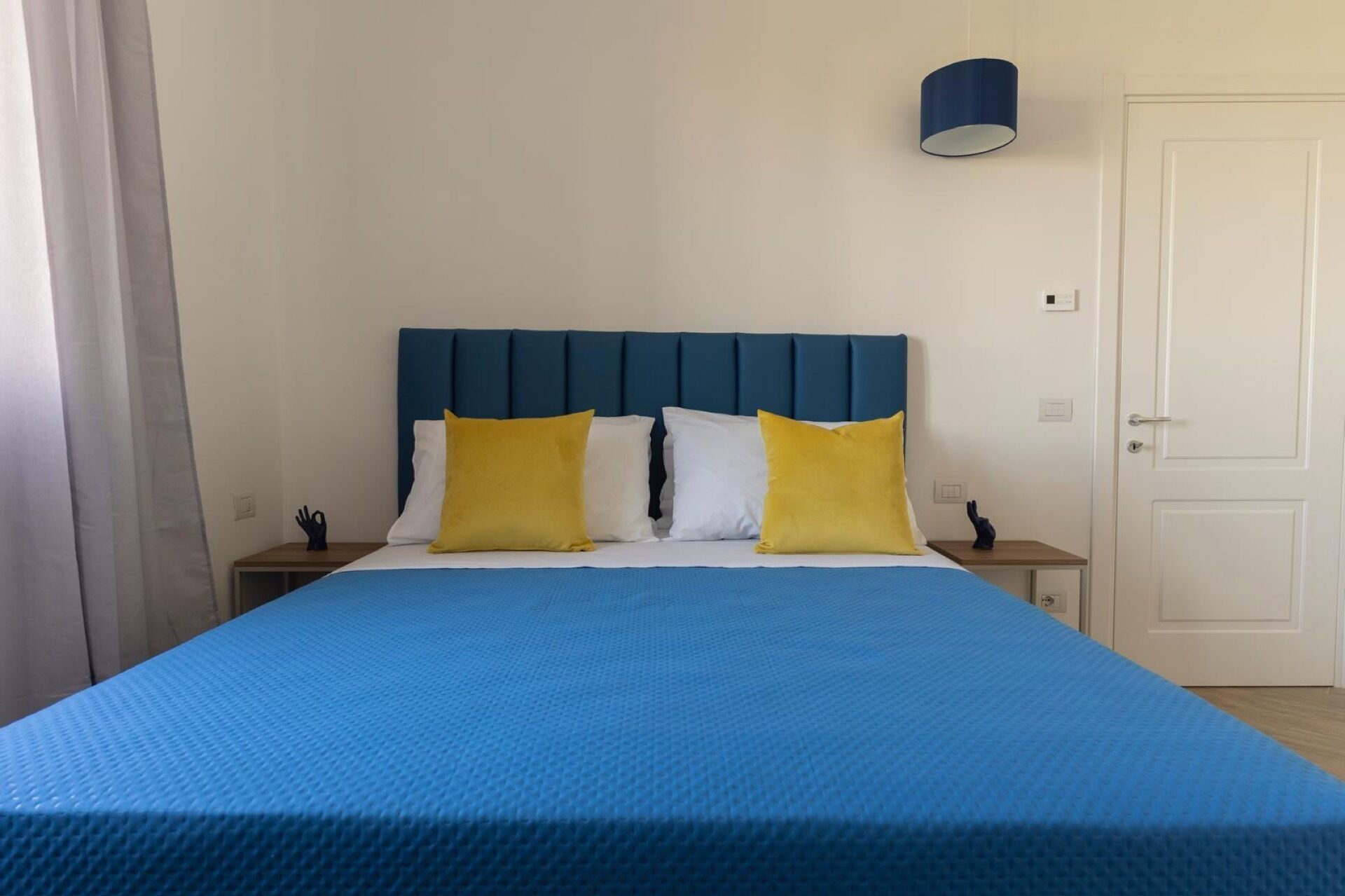 A bed with a blue headboard, white and yellow pillows, and a blue bedspread.