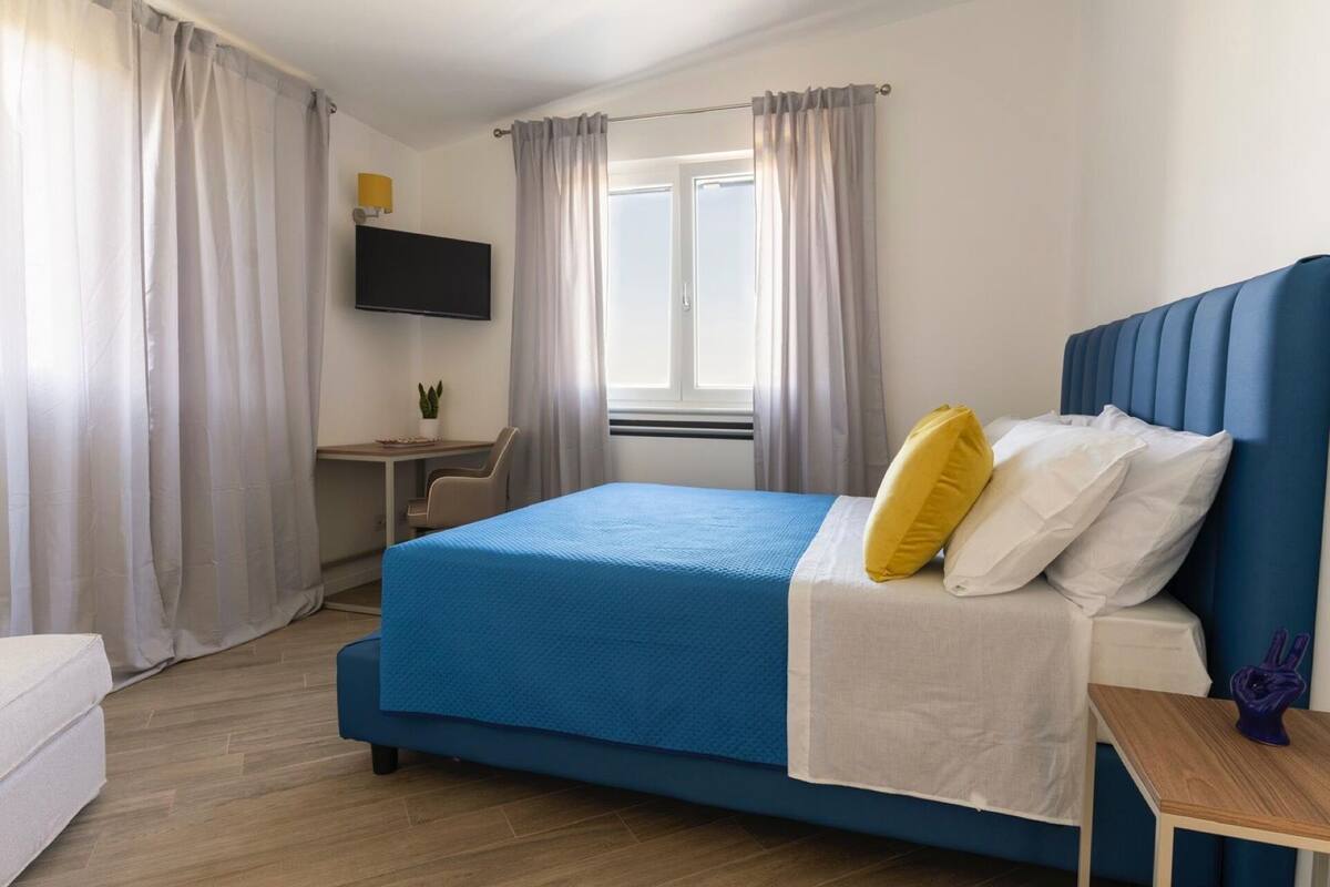 Une chambre à coucher avec un lit, un bureau, une chaise, une télévision et une fenêtre avec des rideaux.