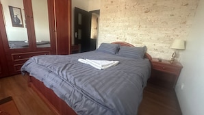 A neatly made bed with a grey duvet and pillows, a wooden nightstand with a lamp, a wooden wardrobe, and a mirror. - 2-bedroom apartment with AC in charming Center Râmnicu Vâlcea (Râmnicu Vâlcea)