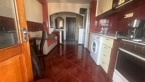 A compact kitchen with a washing machine, a stove, and a dining area with a sofa and a chair. - 2-bedroom apartment with AC in charming Center Râmnicu Vâlcea (Râmnicu Vâlcea)