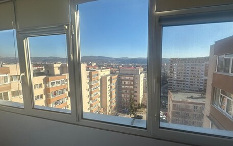 A view from a window with multiple panes, overlooking a cityscape with several multi-story buildings, some with balconies.