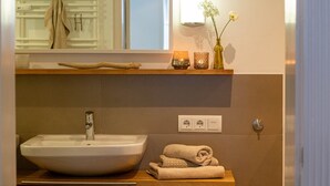 Ein Badezimmer mit einem großzügigen Keramikbecken, einem Handtuchhalter, einer Ablage mit Kerzen und einem Spiegel.