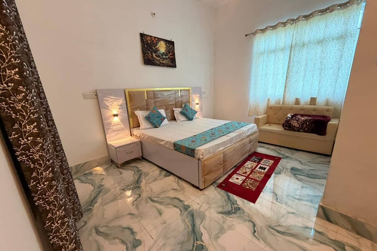 Um quarto com uma cama, mesas de cabeceira, uma obra de arte na parede, um sofá e um tapete estampado.