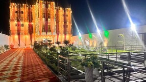 A building with a patterned carpet leading to a gated entrance, surrounded by greenery and illuminated by spotlights. - The Golden Nacre Palace (Bharthana)