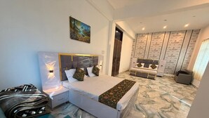 A modern bedroom with a large bed, a nightstand, a blue armchair, and a painting on the wall. - The Golden Nacre Palace (Bharthana)