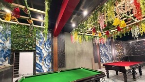 A pool table area with green and red tables, surrounded by decorative plants and a marble-patterned wall. - The Golden Nacre Palace (Bharthana)