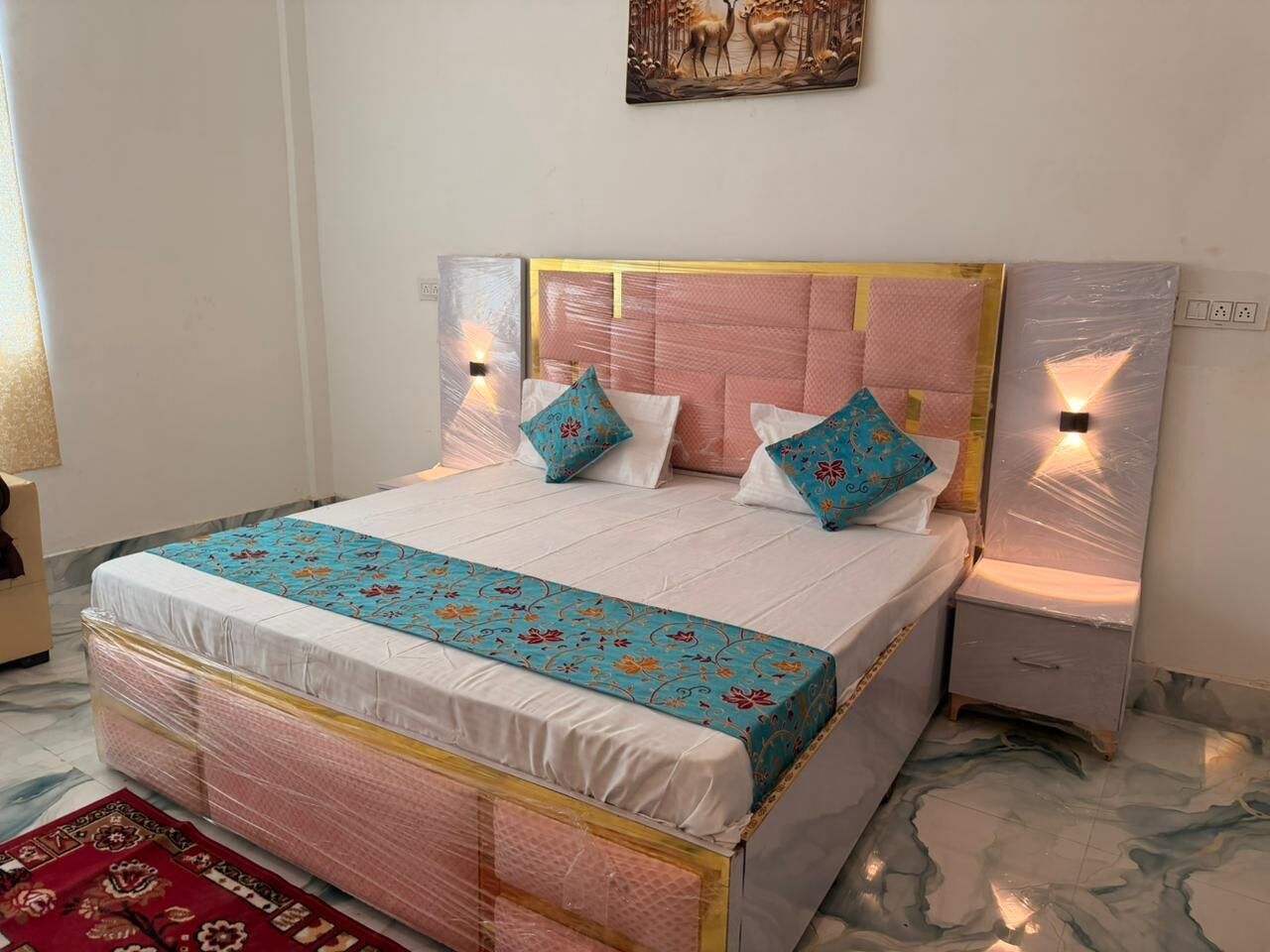 A neatly made bed with a patterned bedspread and pillows, a headboard with a light fixture, and a nightstand with a lamp.