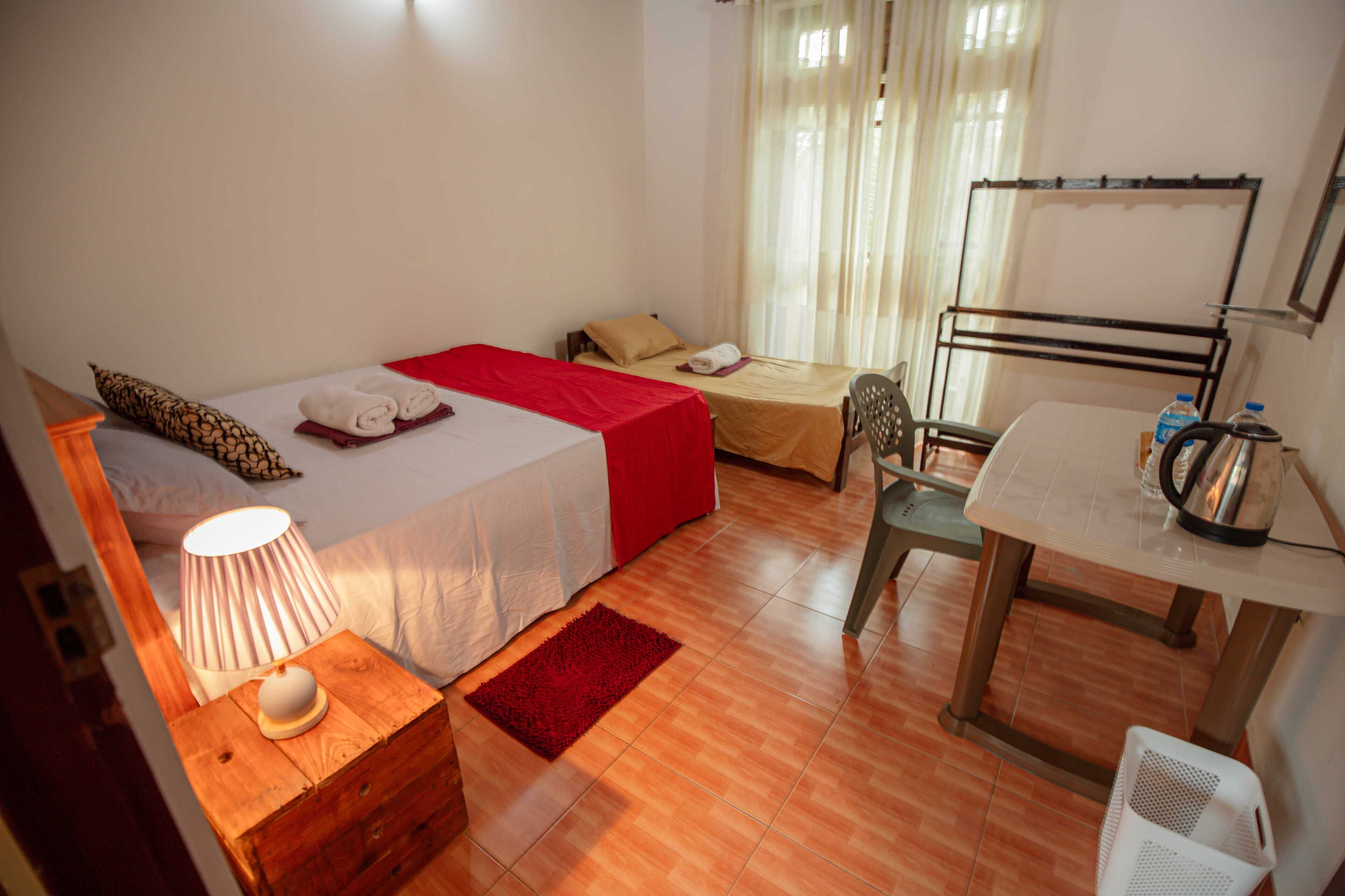 A small, well-lit room with two beds, a desk, and a chair.