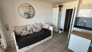 Un espacio habitable compacto con sofá, una pequeña zona de cocina y un espejo en la pared.