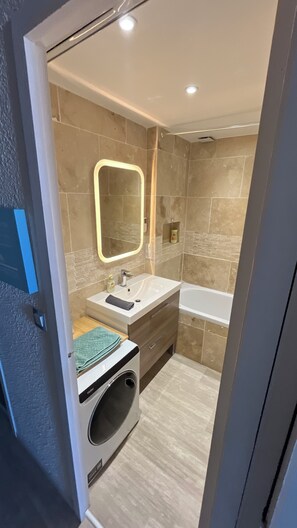 Ein modernes Badezimmer mit einer integrierten Waschmaschine, einem Waschtisch mit Spiegel und einer Badewanne.