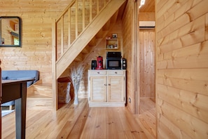 A wooden interior with a staircase, a kitchen area with appliances, and a dining table. - Chalet in Périgord Vert (Sainte-Croix de Mareuil)
