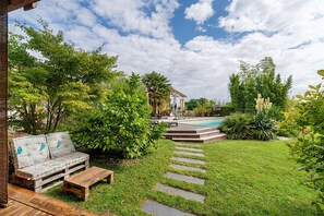 A backyard with a wooden deck, a sofa, a pool, and a stone pathway.