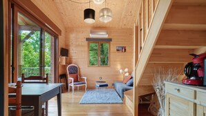 A wooden interior with a dining table, chairs, a sofa, a TV, and a window with a view of greenery. - Chalet in Périgord Vert (Sainte-Croix de Mareuil)