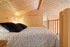 Une chambre dans une cabane en bois, avec un lit, des oreillers et une rambarde en bois.