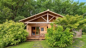 A wooden cabin with a porch, surrounded by lush greenery and stone steps leading to the entrance. - Chalet in Périgord Vert (Sainte-Croix de Mareuil)