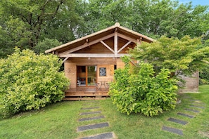 A wooden cabin with a porch, surrounded by lush greenery and stone steps leading to the entrance. - Chalet in Périgord Vert (Sainte-Croix de Mareuil)