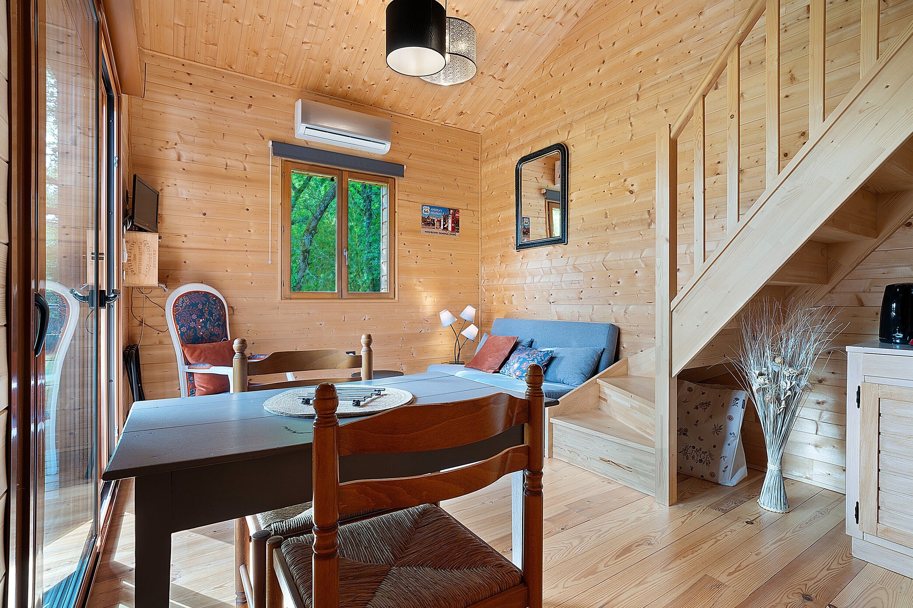 A wooden interior with a dining table, chairs, a sofa, a mirror, and a staircase.