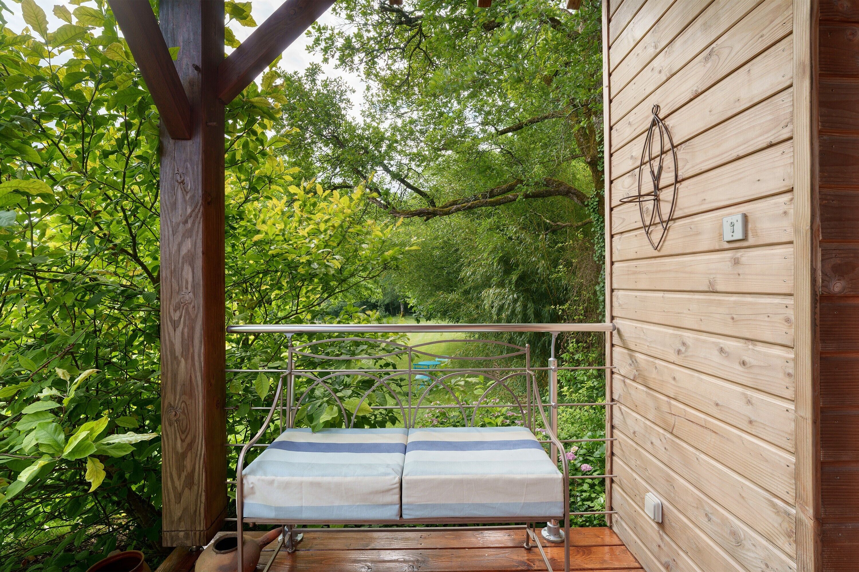 Une terrasse en bois avec un banc en métal et une vue sur un jardin luxuriant.