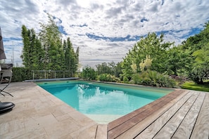 A swimming pool with a wooden deck, surrounded by lush greenery and trees. - Chalet in Périgord Vert (Sainte-Croix de Mareuil)