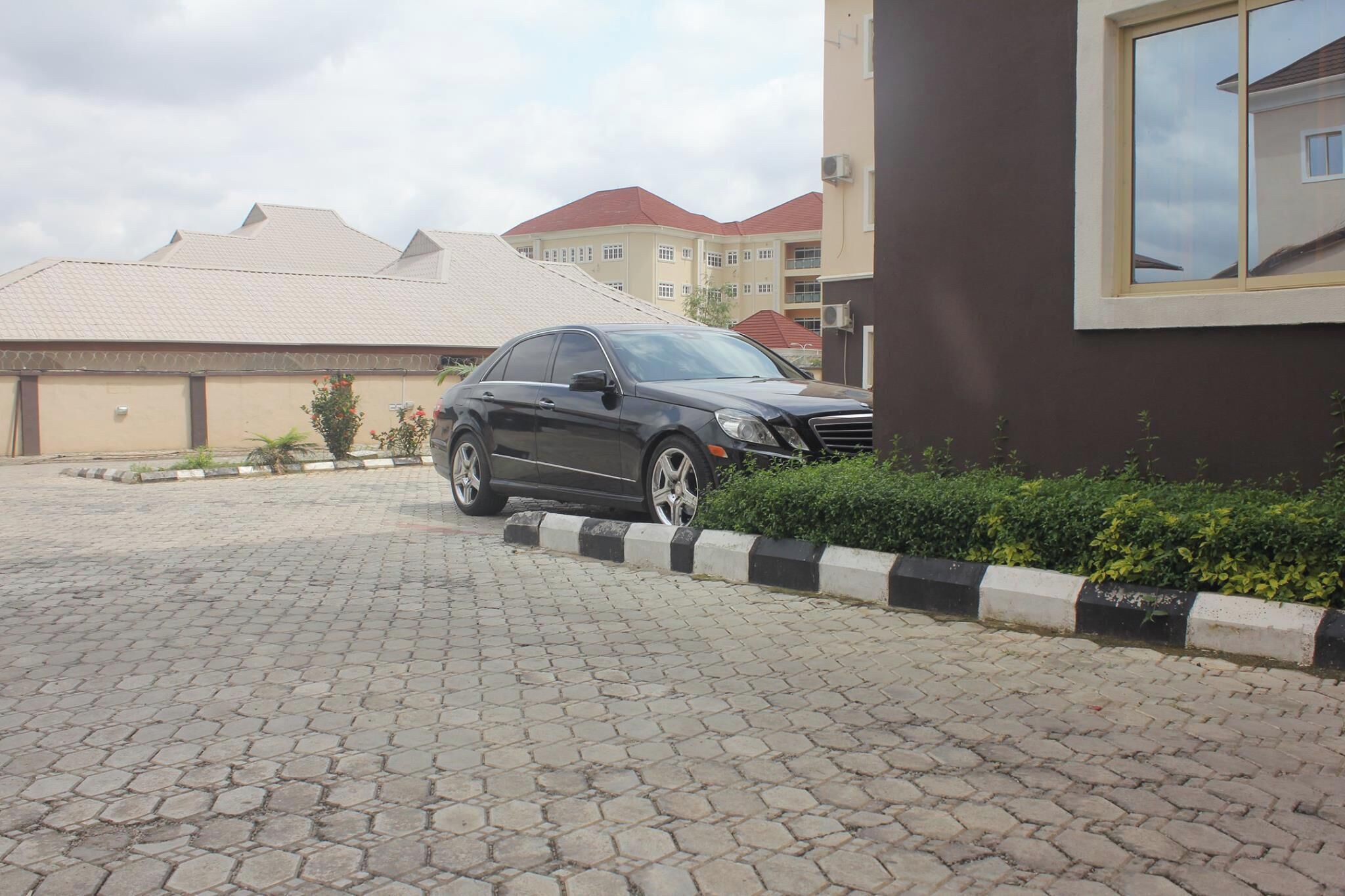 A black car parked on a paved driveway with a building in the background.