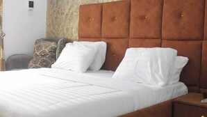 A neatly made bed with white linens, a wooden headboard, and a bedside table with a phone. - Becca Apartment (Abuja)