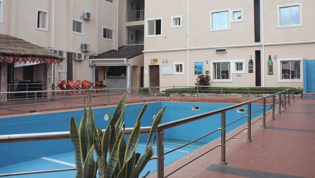 A swimming pool with a metal railing, surrounded by a building with multiple floors and balconies. - Becca Apartment (Abuja)