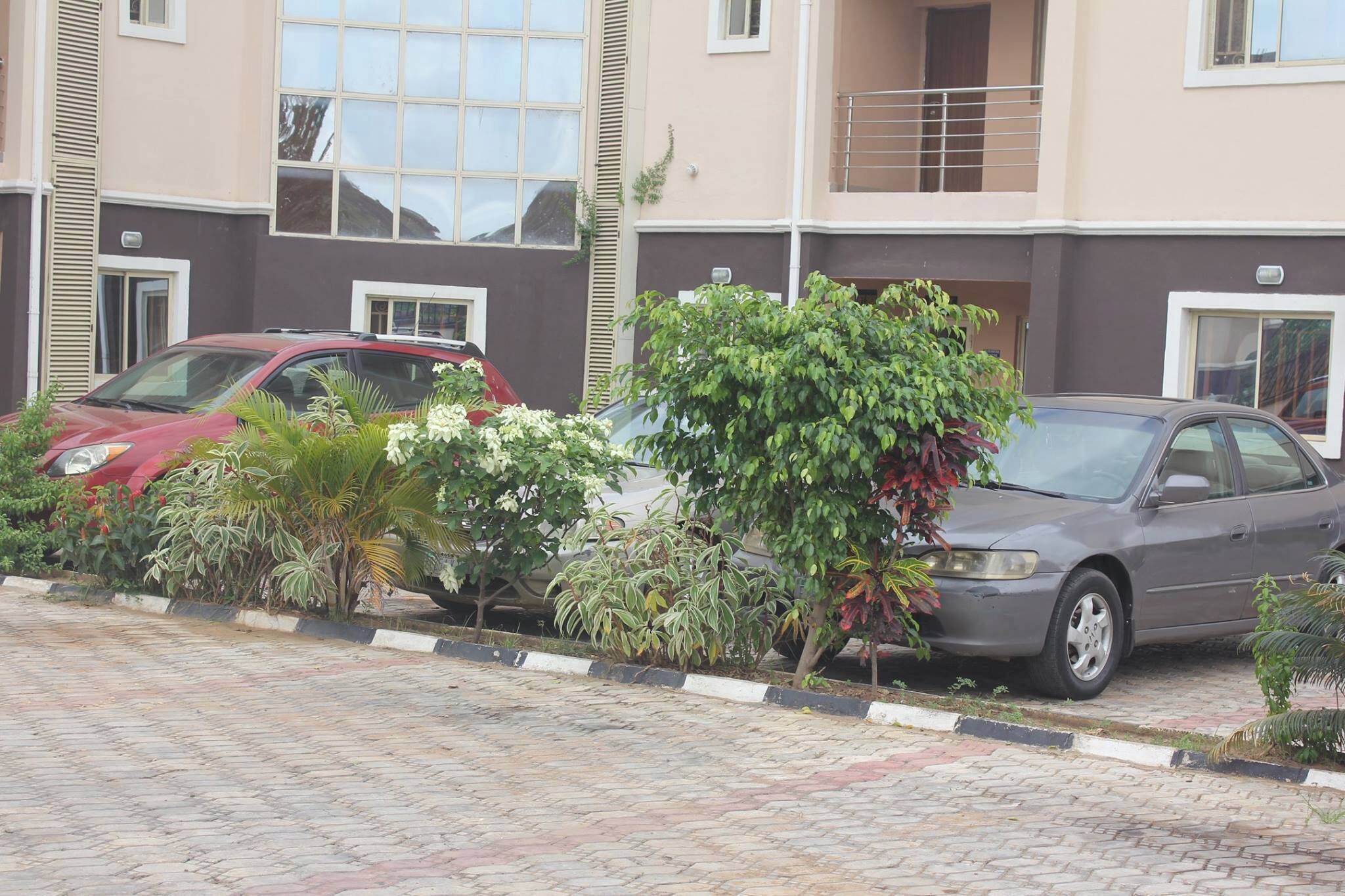 A multi-story residential building with a paved driveway and parked cars.