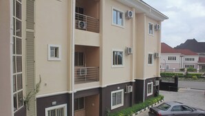 A multi-story residential building with balconies, air conditioning units, and a paved driveway with a parked car. - Becca Apartment (Abuja)