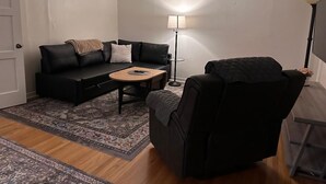 Een gezellige woonkamer met een bank, een fauteuil, een salontafel, een vloerlamp en een kamerkleed met een patroon.