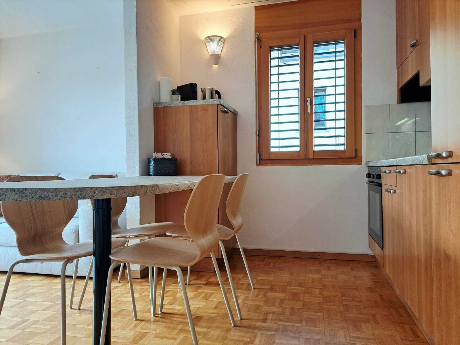 A compact kitchen with wooden cabinets, a granite countertop, and a window with blinds.