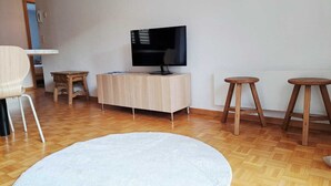 Olohuoneessa on litteänäyttöinen televisio, joka on sijoitettu puiseen kaappiin. Lisäksi huoneessa on kaksi puista jakkaraa, pyöreä valkoinen matto ja puinen tuoli.